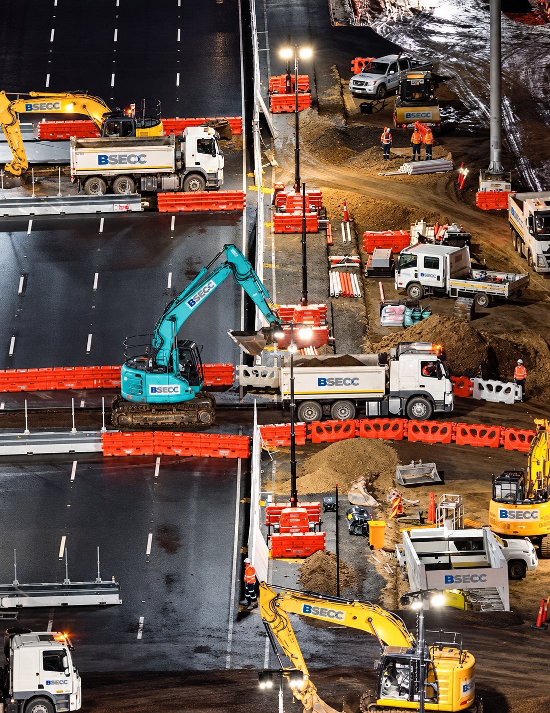 BSECC excavators, tippers and crew working a night shift on the North East Link, orange barriers dividing the work zone from live freeway lanes